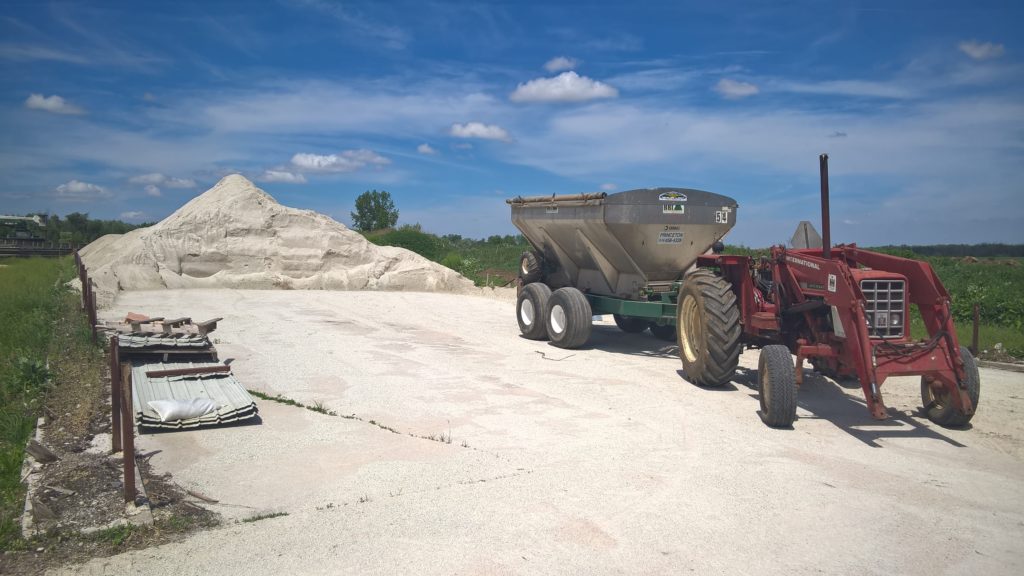 Tractor with fertilizer spreader next to a pile of rock fertilizer